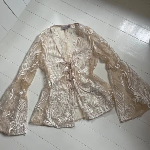 Beige transparent blus med vida ärmar - Säljer en superfin beige transparent blus med broderade mönster och vida trumpetärmar. Blusen har knytning framtill och är i ett tunt, lätt material som ger en lyxig känsla. Aldrig fått tillfälle att använda så jag säljer den. Skicka för fler bilder💞