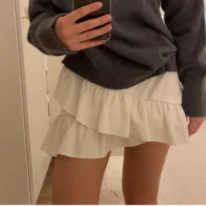 Vit volangkjol - Säljer en superfin vit kjol med volanger och omlottkänsla. Kjolen är kort och har en luftig passform som ger en lätt och somrig vibe. Perfekt att styla med en stickad tröja eller en enkel topp.