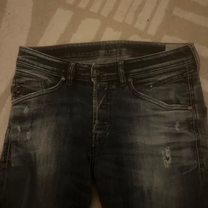 Mörkblåa  slitna jeansbyxor från diesel - Säljer ett par mörkgrå jeansbyxor från diesel  med slitningar och tvättade detaljer. Klassisk femficksmodell med knapp- och dragkedjegylf. Snyggt slitna för en avslappnad look.