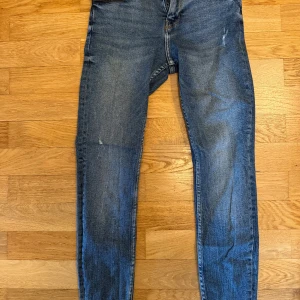Blå jeansbyxor med smal passform - Säljer ett par klassiska blå jeansbyxor med smal passform. Byxorna har fem fickor, normalhög midja och lätt slitna detaljer framtill. Perfekta till vardags och enkla att matcha med olika toppar.