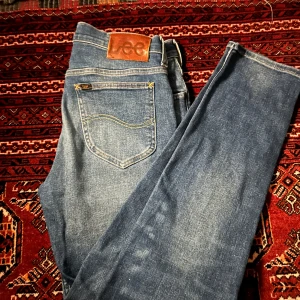 Blå jeansbyxor från Lee - Klassiska blå jeans från Lee med raka ben och normal passform. Jeansen har fem fickor, gylf med dragkedja och Lee-lapp i läder baktill i midjan. Perfekta för en avslappnad stil.
