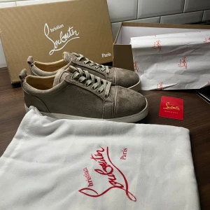 Beige sneakers från Christian Louboutin - Säljer ett par exklusiva beige sneakers från Christian Louboutin med klassisk röd sula och ovandel i mocka. Dom är i beige/grå Perfekta för dig som vill sticka ut med stil, dom är endast testade inomhus därmed är dom i helt nyskick! det som följer med när man köper skorna är box dusbag och ett Christian Louboutin kort, skriv om ni har frågor eller vill ha fler bilder! Kan sänka priset vid snabb affär.🤩🤝 