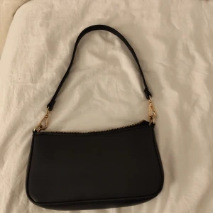 Svart axelväska med gulddetaljer - Snygg svart axelväska med guldfärgade dragkedjor och detaljer. Väskan en yttre ficka med dragkedja och ett rymligt huvudfack med en ficka med dragkedja. Köpt på New yorker,använd fåtal gånger 