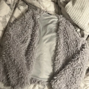 Ljusgrå pälsjacka - Säljer en supermjuk och fluffig ljusgrå pälsjacka. Jackan har lång ärm och är öppen framtill utan synliga knappar eller dragkedja. Perfekt för dig som vill sticka ut och hålla dig varm med stil. Vet ej nypris eftersom att den är begagnad.