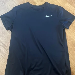 Svart t-shirt från Nike - Säljer en svart t-shirt från Nike med klassisk rund halsringning och liten vit logga på bröstet. Perfekt för träning eller sportiga dagar. Materialet känns lätt och andas bra. Storlek M