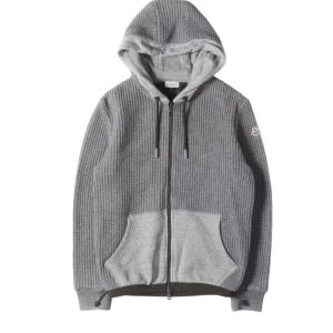Grå stickad hoodie från Moncler - Säljer en grå stickad hoodie från Moncler med dragkedja framtill och två stora fickor. Tröjan har huva med dragsko och ribbade muddar. Perfekt för kyliga dagar och snygg till jeans eller mjukisbyxor.