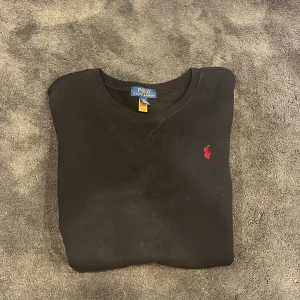 Svart sweatshirt från Polo Ralph Lauren - Säljer en svart sweatshirt från Polo Ralph Lauren med klassisk röd broderad logga på bröstet. Tröjan har rund halsringning och långa ärmar. Perfekt för en stilren och enkel look.