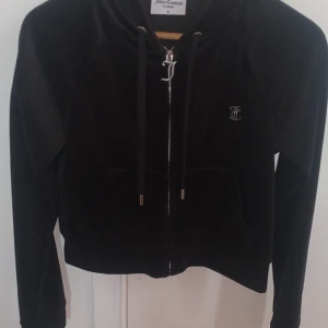 Svart velour hoodie från Juicy Couture - Aldrig använt därför är den dyr, säljer en svart velour hoodie från Juicy Couture med dragkedja och huva. Framsidan har en liten JC-logga och baksidan är dekorerad med glittrande 'Juicy'-text. Jackan har fickor och snörning i huvan.