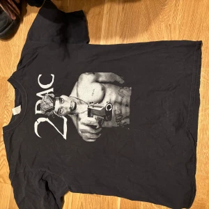 Svart 2Pac t-shirt med tryck - Svart t-shirt med stort tryck av 2Pac på framsidan. T-shirten har klassisk passform och korta ärmar. Perfekt för dig som gillar hiphop och streetwear.
