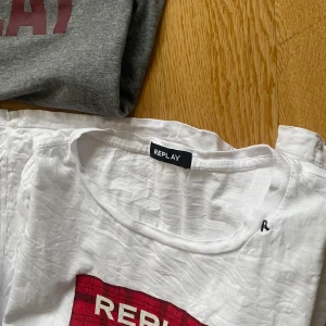 Vit t-shirt från Replay med röd logga - Vit t-shirt från Replay med röd logga framtill. Klassisk rund halsringning och normal passform. Perfekt för en avslappnad stil och enkel att matcha med jeans eller shorts.