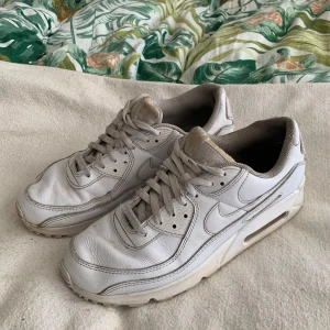 Vita Nike Air Max sneakers - Säljer ett par klassiska vita Nike Air Max sneakers med synlig luftbubbla i sulan. Skorna har snörning och är tillverkade i skinn med diskreta Nike-loggor på sidorna och hälen. Perfekta för dig som gillar en sportig och tidlös stil.