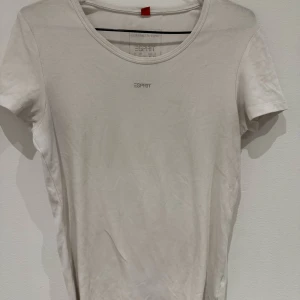 Vit t-shirt från Esprit - Klassisk vit t-shirt från Esprit med rund halsringning och diskret logga framtill. Enkel och stilren design som passar till det mesta. Tillverkad i mjuk bomull för en skön känsla hela dagen.