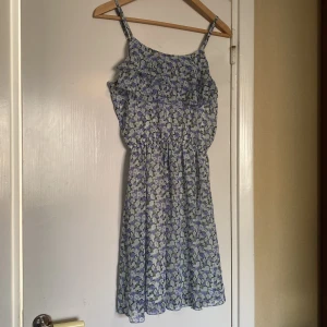 Blommig ljusblå sommarklänning med volang - Söt ljusblå klänning med blommigt mönster och volangdetalj upptill. Axelbandslös modell med avslappnad passform🌼Strl 164