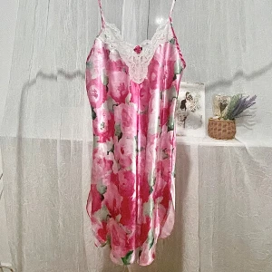 Blommig satin slipklänning med spets - Säljer en söt slipklänning i glansigt satinmaterial med rosa och grönt blommönster. Klänningen har tunna axelband och vit spetsdetalj vid urringningen. Perfekt för sommarens varma dagar eller som nattlinne.