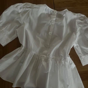 Blus Med Puffärm - Supersöt topp med puffärm och vidare vid midjan. Knappar baktill. 