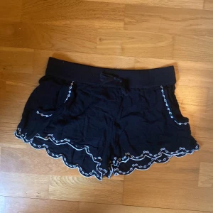 Svarta shorts med broderade detaljer - Svarta shorts med vita broderade kanter och volang längst ner. Shorts med resår i midjan och snörning framtill. Perfekta för sommaren och har en avslappnad passform. Passar xxs-m då den är streching 