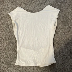 Vit topp från Gina Tricot - Säljer en stilren vit topp från Gina Tricot. Den är ärmlös och har en enkel design som passar perfekt till olika outfits. Toppen är gjord i ett mjukt och bekvämt material.