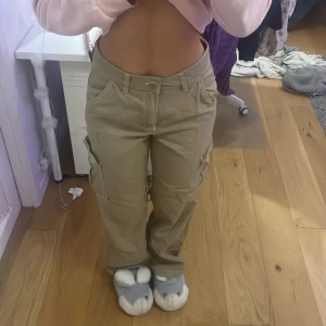 Beige cargobyxor från H&M Divided - Snygga beige cargobyxor från H&M Divided med flera praktiska fickor. Byxorna har en avslappnad passform och är perfekta för en casual look. Tillverkade i ett slitstarkt material som ger en cool och bekväm stil. Jeansen har en vit sömn som jag tycker är väldigt stiligt! Dem är high waisted och lite baggy.😊