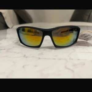 Svarta solglasögon med spegelglas från Future eyewear  - Snygga svarta solglasögon med spegelglas som skiftar i gult och blått. Perfekta för en cool look och skyddar mot solen. De har en modern och sportig design som passar bra till olika aktiviteter.