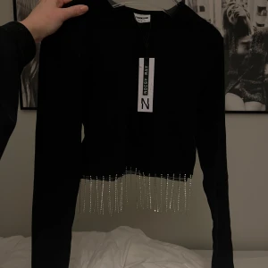 Svart tröja med pärldetaljer från Noisy May - Snygg svart tröja från Noisy May med långa ärmar och coola pärldetaljer som hänger från nederkanten. Perfekt för att ge din outfit en extra touch. 🖤
