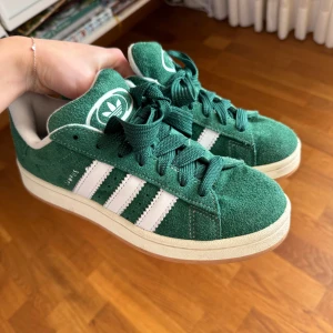 Adidas Campus 00  - Säljer dessa skitsnygga Adidas Campus 00 som är gröna i storlek 38 2/3. Har endast använts fåtal gånger så är i superbra skick som nya! Smalt grönt skosnöre kommer med och även det gröna breda på bilden och vitt brett. 
