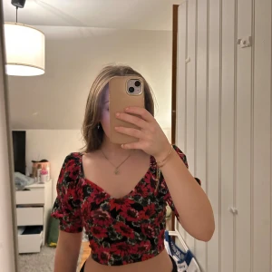 Blommig croppad topp - Croppad blommig topp med puff ärmar och är v ringad, storlek xs