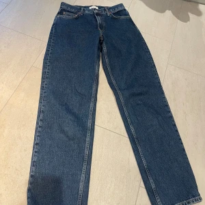 Blå jeans från Gina tricot - Snygga blå jeans med klassisk femficksdesign och knappgylf. De har en rak passform och är perfekta för en avslappnad stil. Märkeslappen i brunt läder ger en extra touch.