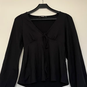Svart långärmad topp från Bikbok - Toppen har en v-ringning och knytning framtill. Den ger en väldigt fin siluett och form. Säljer den pga den är för kort på ärmarna (jag är 174)💕