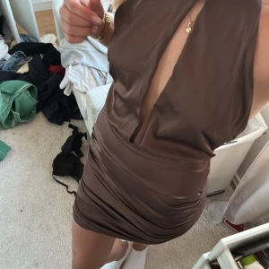 Brun klänning från Bianca Nelly - Snygg brun klänning från Bianca Nelly med djup v-ringning och tight passform. Perfekt för en kväll ute. Klänningen är ärmlös och har en kort längd som ger en elegant look.