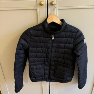 Svart dunjacka från Moncler Lana 12a - Säljer en snygg svart dunjacka från Moncler med dragkedja och knappar på fickorna. Jackan har en quiltad design och långa ärmar. Perfekt för kyligare dagar! 🖤mycket gott skick 