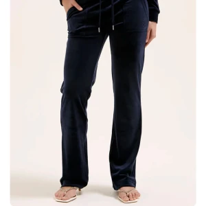 Mörkblå juicy couture byxor - Snygga mörkblå byxor i mjuk velour med en avslappnad passform. Byxorna har dragsko i midjan och utsvängda ben, perfekta för en bekväm stil. Passar bra till både vardag och avslappnade tillfällen. Ena metall ringen har ramlat av där fram men det är inget man märker av. 