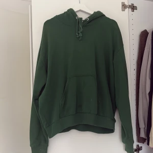 Grön hoodie från Weekday - Säljer en grön hoodie från Weekday i storlek S. Den har en klassisk design med en stor ficka framtill och justerbar huva med snören. Perfekt för en avslappnad stil.