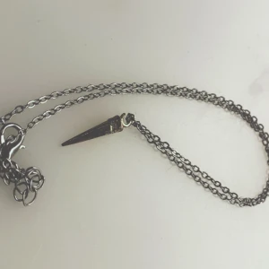 Halsband med konformad hängsmycke - Snyggt halsband med en konformad hängsmycke i metall. Kedjan är tunn och elegant, vilket ger en stilren look. Perfekt för att lägga till en edgy touch till din outfit.