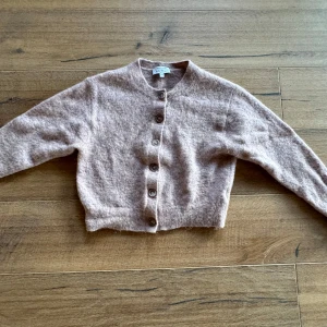 Beige kofta från & Other Stories - Säljer en mysig beige kofta från & Other Stories. Den har en klassisk design med knappar framtill och är perfekt för kyligare dagar. Koftan är tillverkad i ett mjukt material som ger en skön känsla mot huden. 