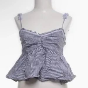 Randig blus med volangdetaljer - Söt blus med smala axelband och volangdetaljer. Blusen har ett randigt mönster i blått och vitt och är perfekt för varma dagar.