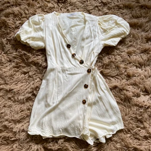 Offwhite klänning med knappar - Vit kortklänning med puffiga kortärmar. Fint skick. Står att det är storlek S, men skulle nog säga att den mer är XS