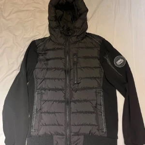 Svart pufferjacka från Supply  - Säljer en svart pufferjacka från Superdry med huva och dragkedja. Jackan har långa ärmar och en quiltad design. Perfekt för kyligare dagar. 🖤