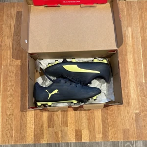 Svarta fotbollsskor från Puma - Snygga svarta fotbollsskor från Puma med gula detaljer. Skorna har snörning och är designade för att ge bra grepp på planen. Perfekta för fotbollsspelare som vill ha stil och funktionalitet. Perfekt om din son vill testa på fotboll med ett par forbollskor i mycket bra skick.