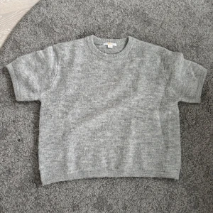 Grå stickad tre kvartsärmad tröja - Säljer en stilren grå stickad tröja. Tröjan har en rund halsringning och korta ärmar, perfekt för lager på lager-stil. Den är mjuk och bekväm, idealisk för kyligare dagar.