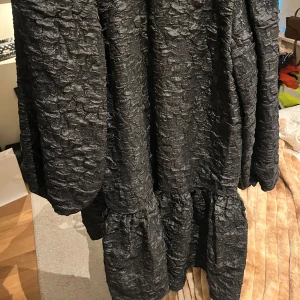 Svart klänning med knytning - Snygg svart klänning med texturerat tyg och knytning i ryggen. Den har långa ärmar och en lös passform som ger en avslappnad look. Perfekt för en stilren outfit.