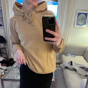 Beige hoodie från Gina Tricot - Säljer en snygg beige hoodie från Gina Tricot. Den har en bekväm passform med långa ärmar och en justerbar huva med knytband. Lite sliten i snörena, men går givetvis att fixa till!