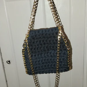Svart virkad väska med guldkedja - Snygg svart virkad väska med en iögonfallande guldkedja. Perfekt för att ge din outfit en trendig touch. Väskan har en unik textur och stil som gör den till ett måste i garderoben.