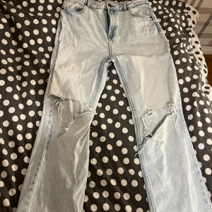 Ljusa jeans med slitningar - Säljer ett par ljusa jeans med coola slitningar på knäna. De har en klassisk femficksdesign och knappgylf. Perfekta för en avslappnad stil.