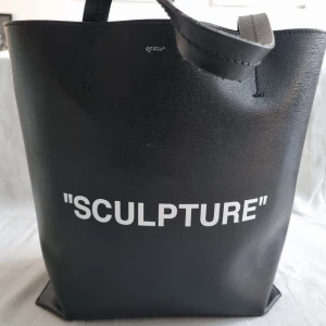 Svart axelväska från Off-White - sculpture serien  - Svart axelväska från Off-White med texten 'SCULPTURE' tryckt i vitt. Väskan har en justerbar axelrem och är tillverkad i slitstarkt material. 2 st axelband.  Ett smalt i läder och ett med off white texten. Båda avtagbara.  Nyskick och Äkta off white. Nypris 10500