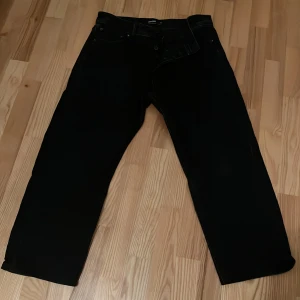 Svarta jeans från Jack & Jones - Säljer ett par svarta jeans från Jack & Jones i modellen Loose/Eddie. De har en lös passform och är tillverkade av kvalitativ bomull. Perfekta för en avslappnad stil. Uppfollade ca 2 cm, så längden är kortare än 32. 