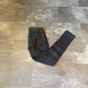 Svarta jeans från Nudie Jeans - Säljer ett par svarta jeans från Nudie Jeans i storlek 30/32. Jeansen har klassisk femficksdesign, silverfärgade nitar och smal passform hela vägen ner. Perfekta om du gillar en stilren och enkel look.