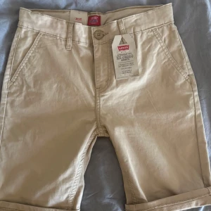Beige straight fit chino shorts Levi's - Snygga beige straight fit XX chino shorts från Levi's med stretch och justerbar midja. Klassisk design med raka ben, fickor fram och bak samt knapp och dragkedja. Köpta i helgen då jag trodde de skulle passsa, men satt alldeless för tajt på mig som är 16/17 år. Säljs för 360 kr, 430 kr nypris.