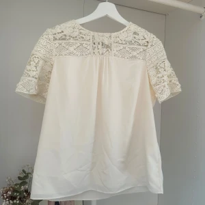 Vit spetsblus från Hobbs London - Superfin vit blus från Hobbs London med vackra spetsdetaljer över axlar och ärmar. Blusen har korta ärmar och materialet känns mjukt och lyxigt.
