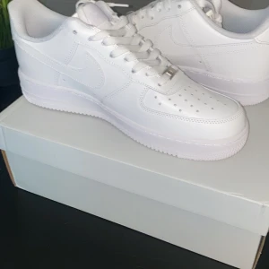 Air Force 1 - Klassiska Nike Air Force 1 i helvitt skinn med lågt skaft och vit sula. Snygg och clean design med perforerade detaljer på tån och ikonisk swoosh på sidan. Perfekta för dig som vill ha en tidlös och fräsch sneaker till din outfit. Storlek 42.5 och helt oanvända!!