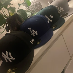 New Era kepsar NY, LA & Oakland - Fyra klassiska New Era 59Fifty kepsar med broderade loggor: svart NY Yankees, blå LA Dodgers, grön Oakland A's och grå LA Dodgers. Alla har platt skärm och sticker ut med sina tydliga lagloggor framtill. Perfekt för dig som gillar streetwear och sport.